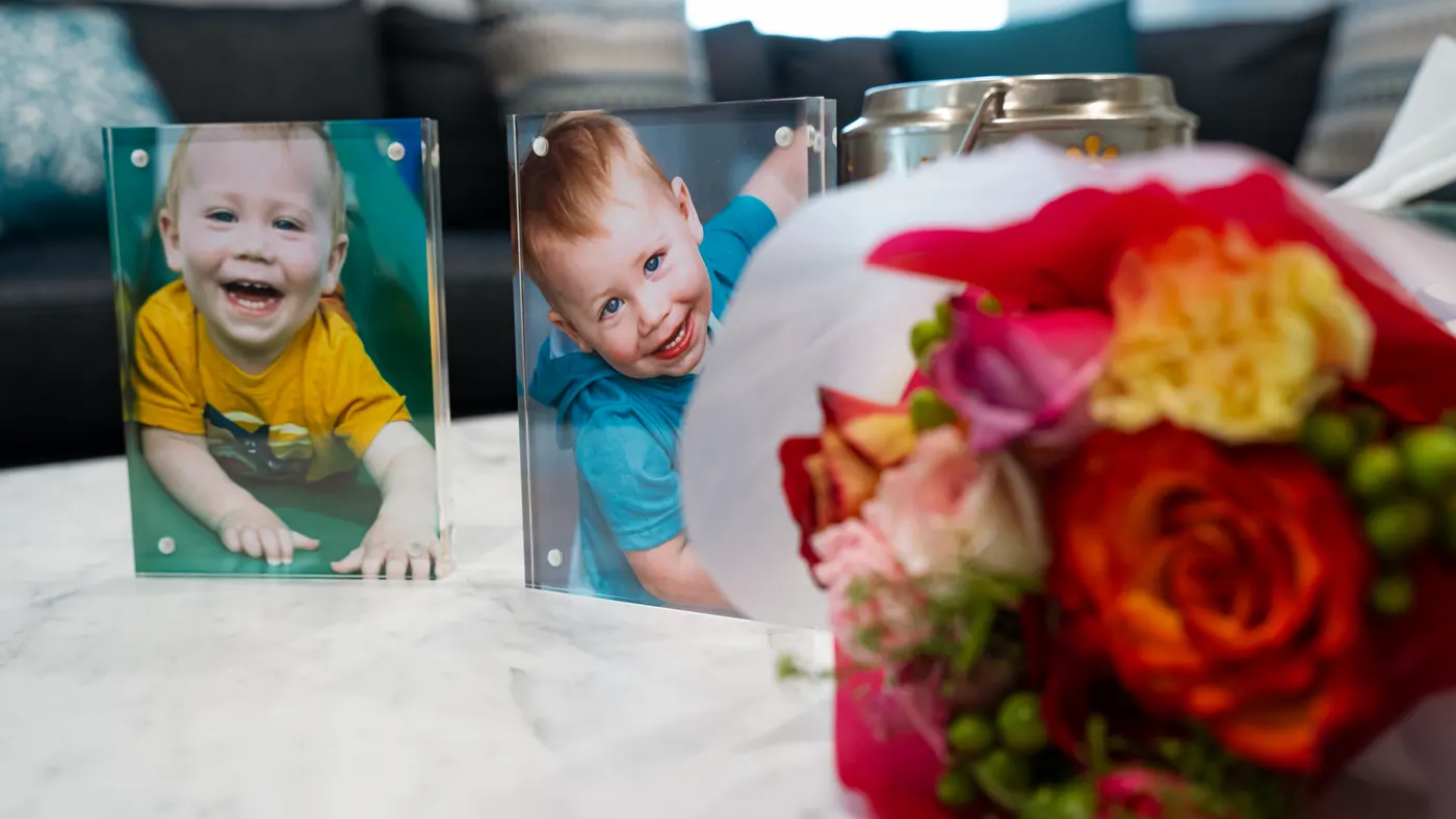 Two framed photographs of a smiling young child stand beside a bouquet of flowers.