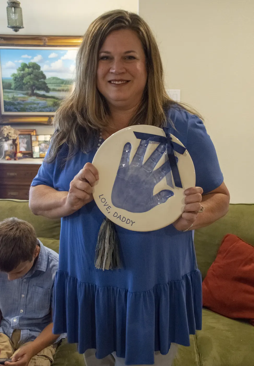 A smiling woman holds up a round keepsake plate pressed with a handprint.